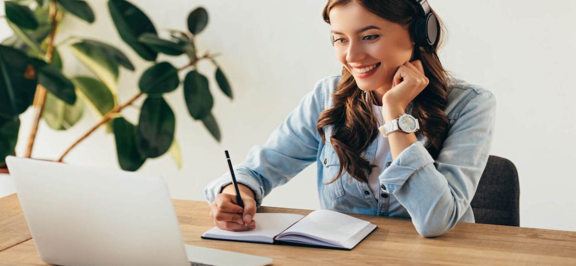 Woman sitting at wooden desk watching a webinar on laptop.