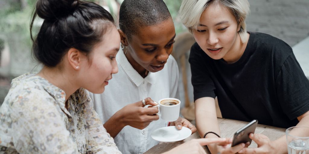 Diverse group of friends checking social media on mobile phone in cafe