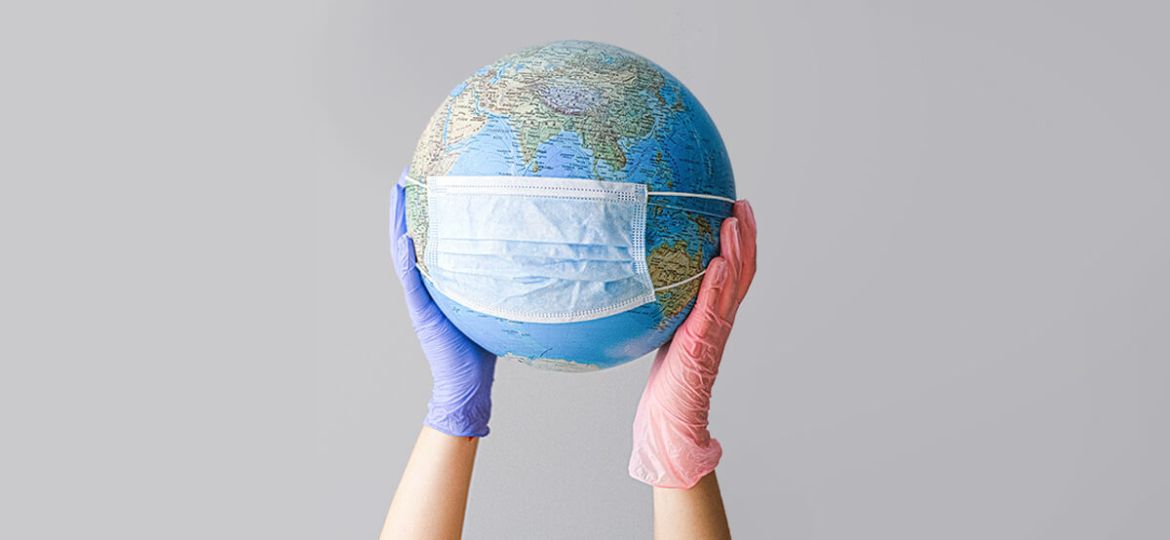 Person wearing rubber gloves holding up globe with mask on it