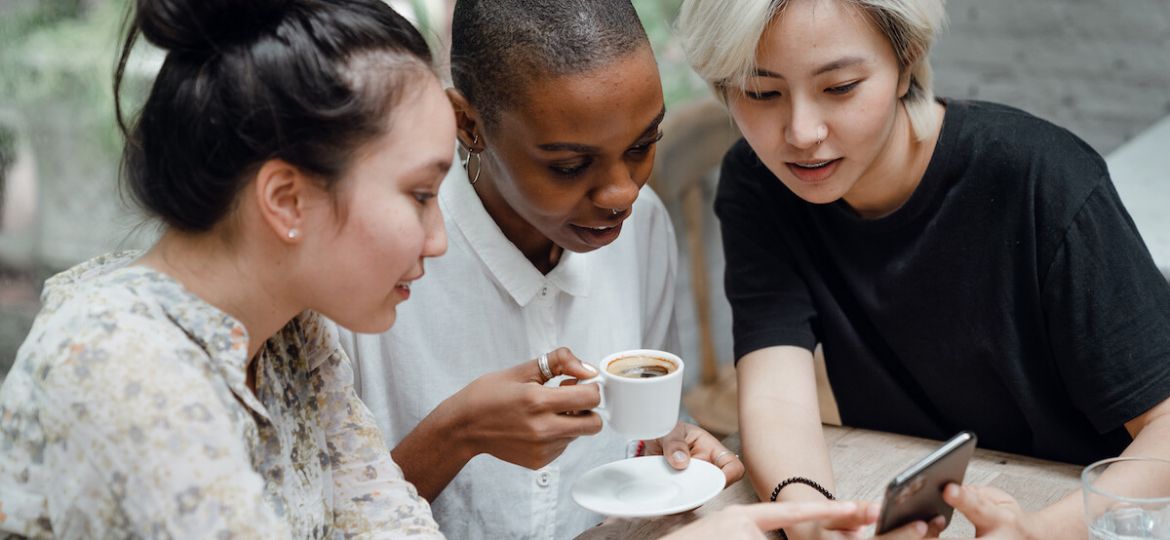 Diverse female friends checking social media on mobile phone in cafe