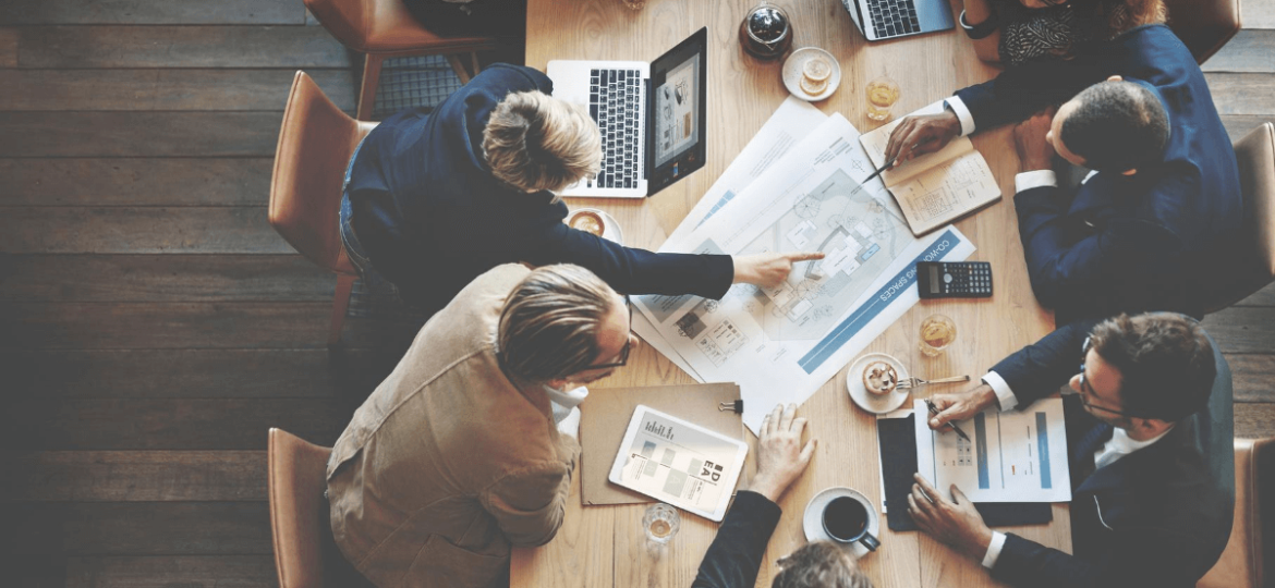 group of people at conference table with laptops and plans