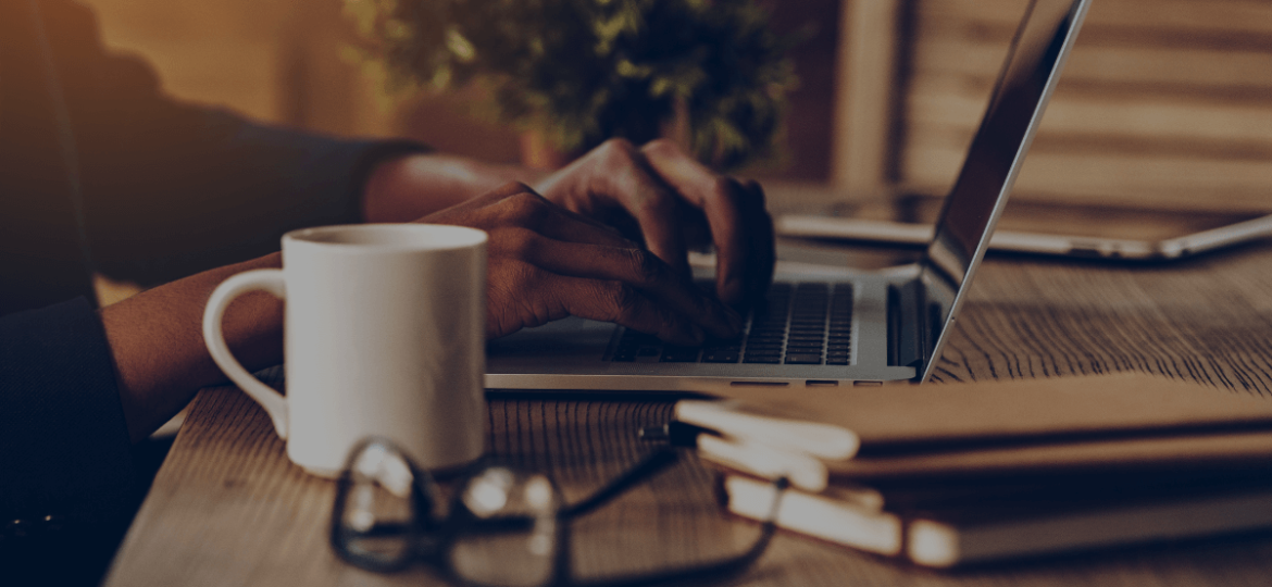 Person typing on laptop with coffee, glasses, and books on the desk